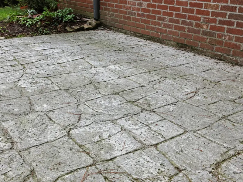 Faded, chalky stamped patio with worn high spots and mildew in the joints beside a red brick wall