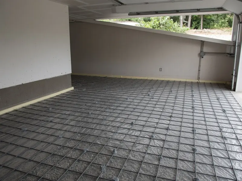 Garage stripped for a new floor, with plastic vapor barrier over a gravel base, a rebar grid on chairs and foam isolation strips along the walls